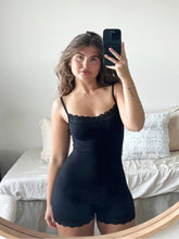 Woman in a black Florence by Mills romper with lace trim, taking a mirror selfie.