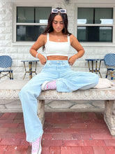 Young woman in a casual outfit with white crop top, light jeans, and pink shoes, sitting on an ornate bench.