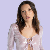 Woman wearing a lavender sequin top with hoop earrings, posing against a light purple background.